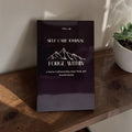 Forge Within Men’s Self‑Care Journal — dark journal with white mountain line art and craftsmanship subtitle, styled on a wooden surface beside a white pot succulent in soft natural light.