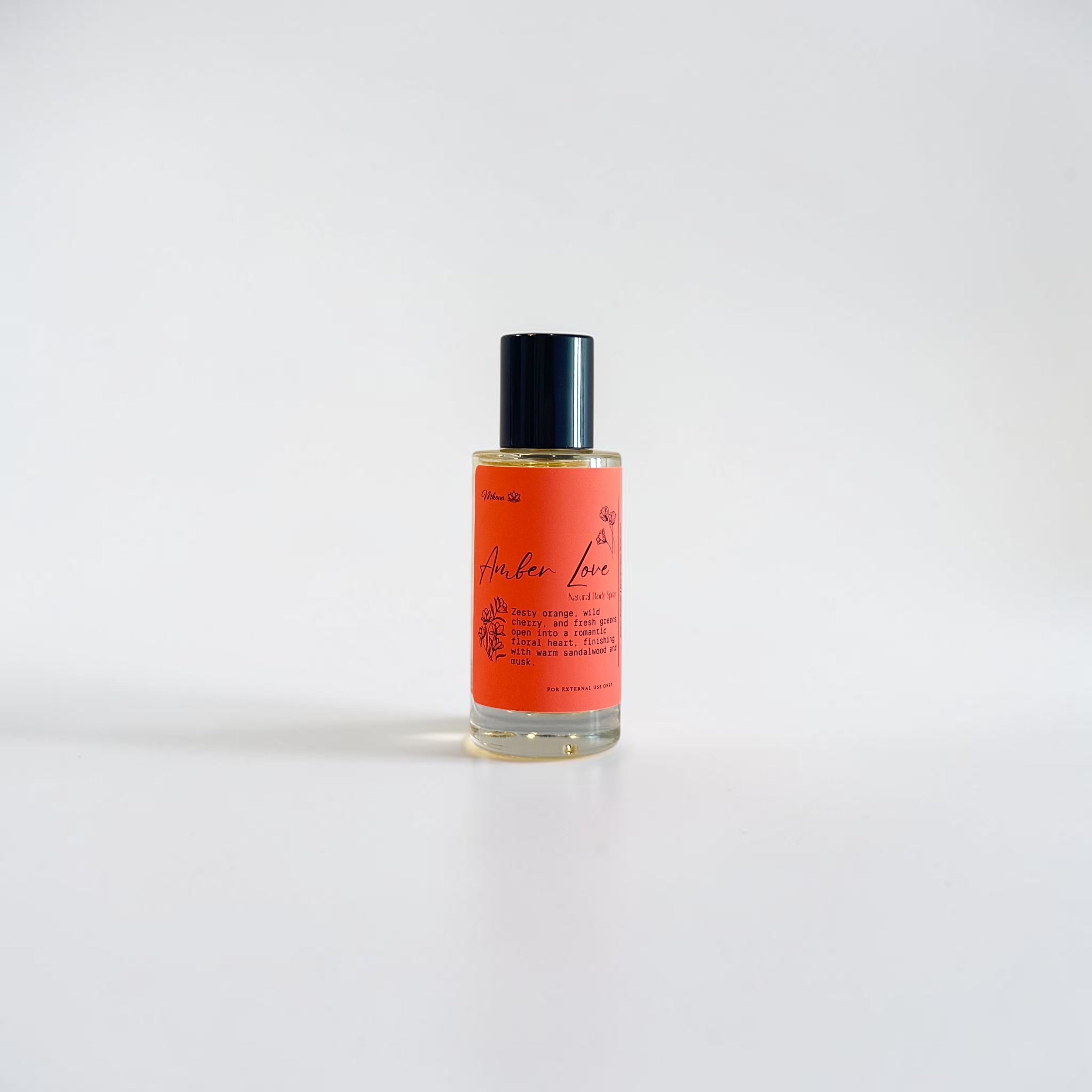 Amber Love Body Oil — bright orange, leafy greens, wild cherry, jasmine, freesia, rose, honeysuckle, sandalwood, and warm musk photographed on a clean white background.