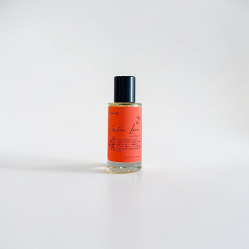 Amber Love Body Oil — bright orange, leafy greens, wild cherry, jasmine, freesia, rose, honeysuckle, sandalwood, and warm musk photographed on a clean white background.