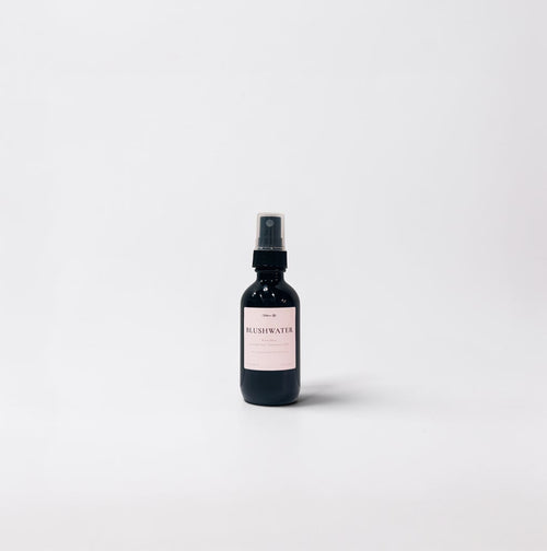 Blushwater 2oz Room Spray — juicy peach, delicate lychee, airy white tea, and soft florals in a black glass bottle on a clean white background.