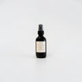 Citrus Basil Tea 2oz Room Spray — black glass bottle with a beige label featuring orange leaf, lime, and tea blend notes, styled on a light surface in soft natural light.