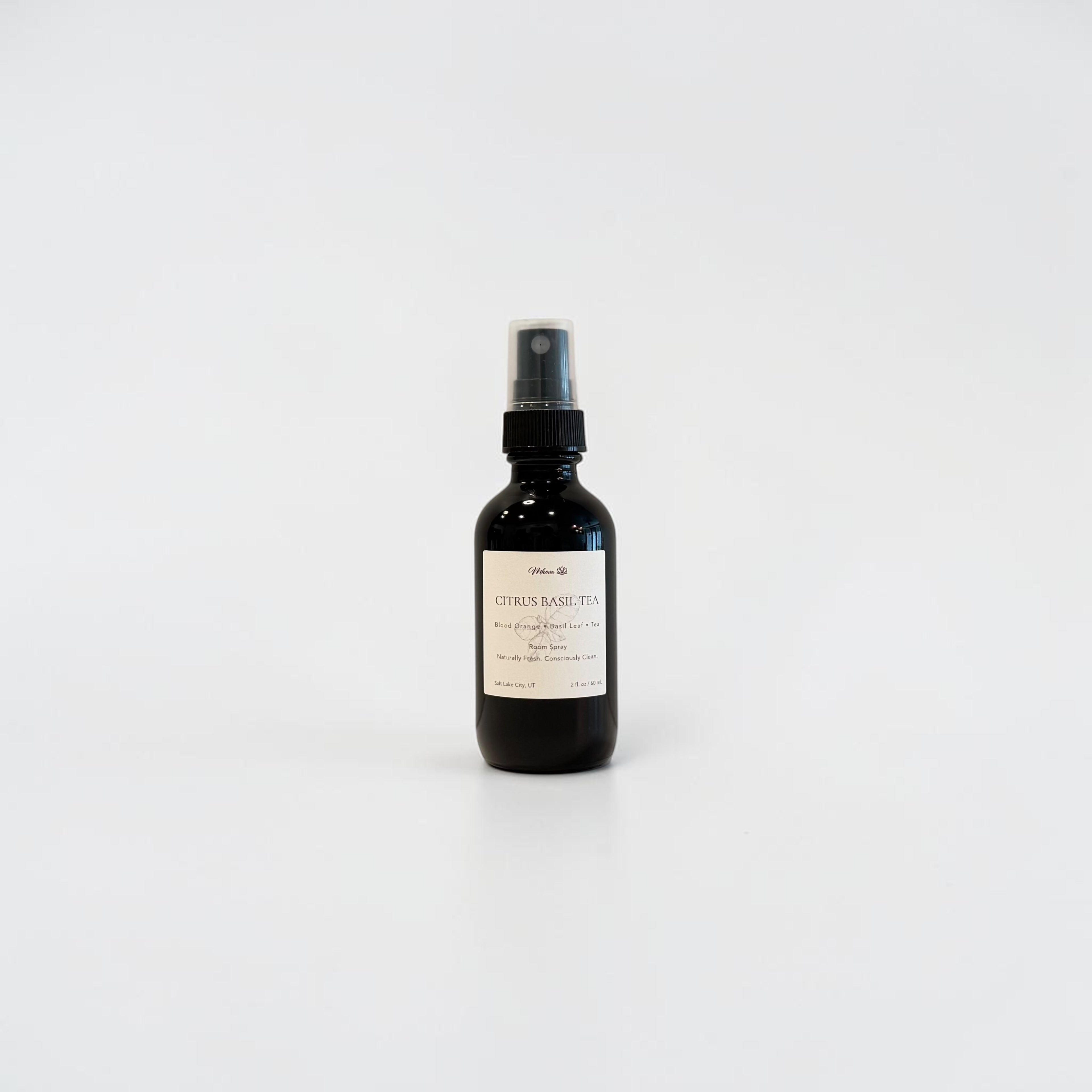 Citrus Basil Tea 2oz Room Spray — black glass bottle with a beige label featuring orange leaf, lime, and tea blend notes, styled on a light surface in soft natural light.